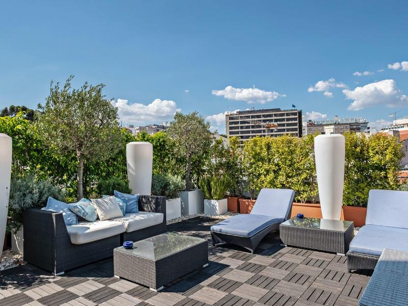 Modern terrace with lounge furniture, large plant vases, and blue sky.