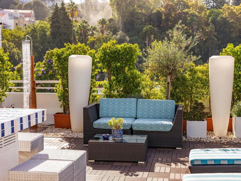 Modern outdoor area with seating furniture and plants against green landscape.