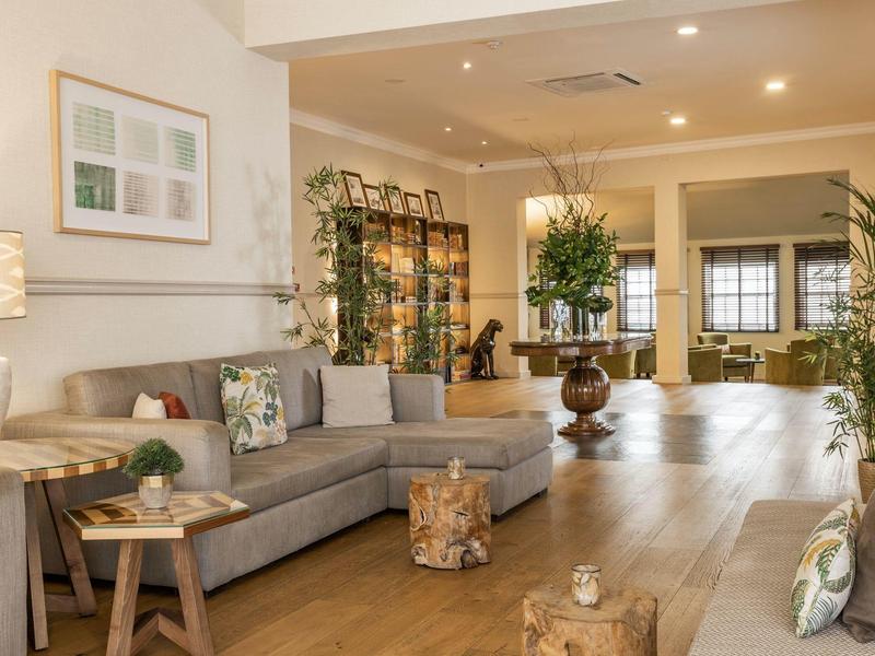 Modern living area with gray corner sofa, wooden floor, and plants in a hotel.