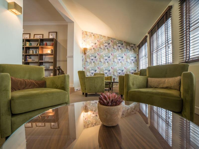 Modern green seating around a reflective glass table in a bright hotel lounge area
