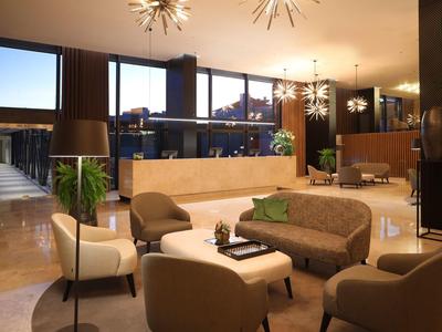 Modern hotel lobby with seating areas, plants, and large windows.
