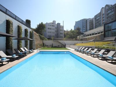Piscina all'aperto moderna con sdraio e edifici circostanti in una giornata di sole.