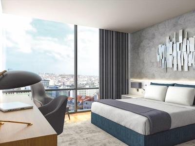 Modern hotel room with large bed, desk, chair, and panoramic windows overlooking the city.