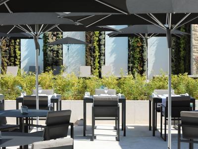Outdoor seating area of a hotel with white tables, black chairs, and large umbrellas.