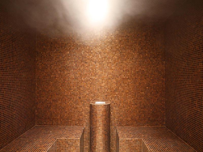 Steam room with brown mosaic tiles and central seating pedestal under bright light