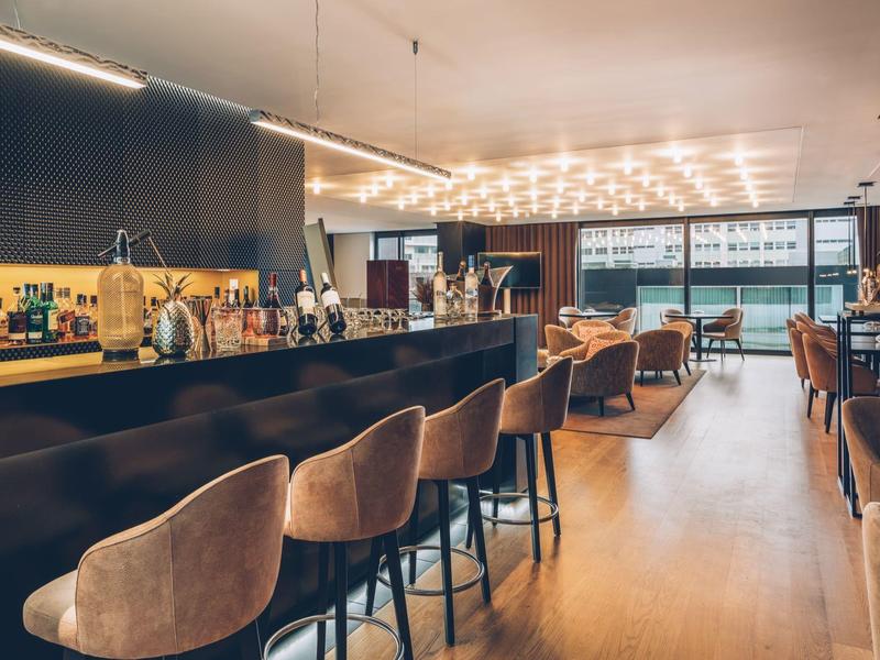 Modern hotel bar with wooden floors, bar stools, and cozy seating areas in daylight
