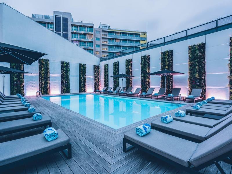 Modern outdoor pool with lounge chairs and urban backdrop at dusk.