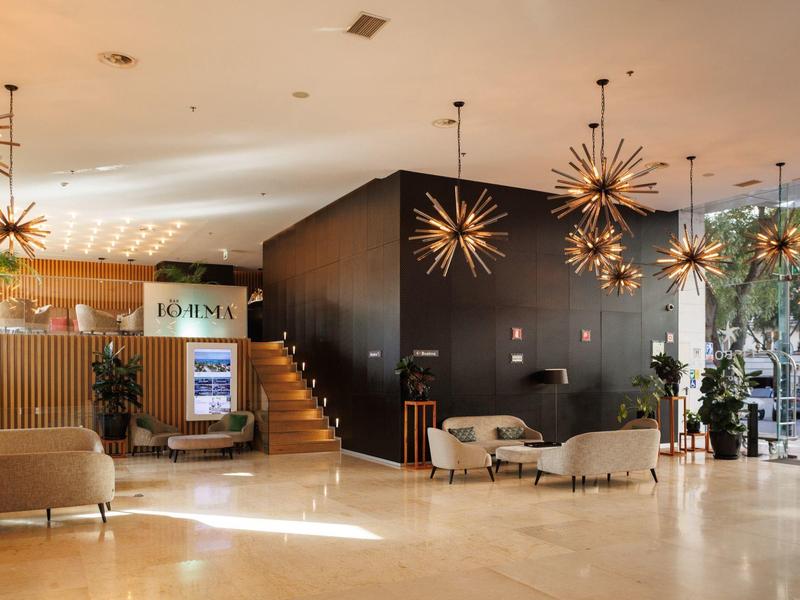 Bright hotel lobby with modern lighting and cozy seating areas next to a staircase.