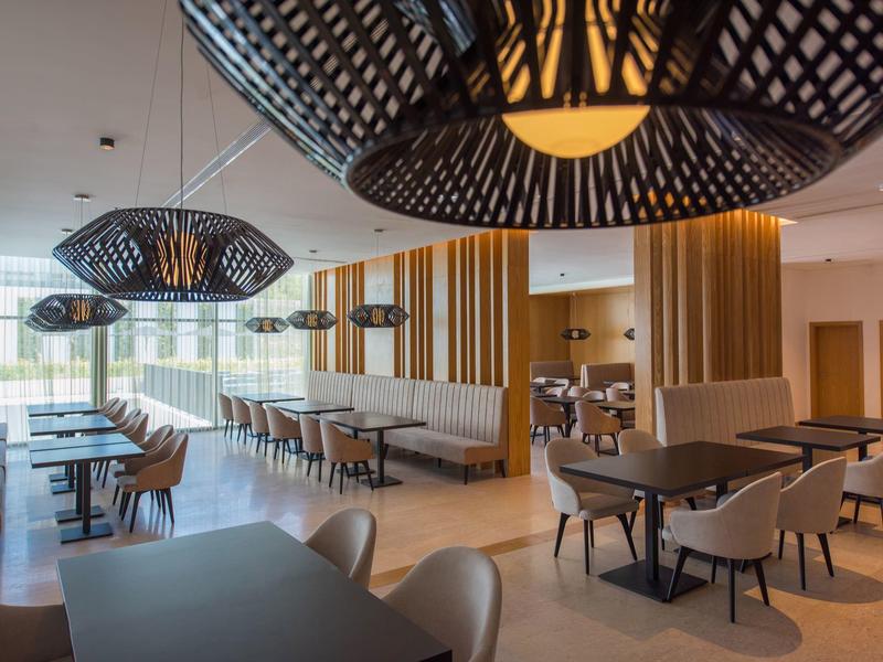 Modern hotel restaurant with wood accents, gray tables and chairs, and large designer lamps.