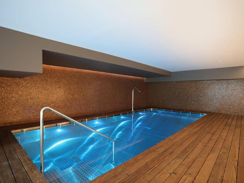 Modern indoor pool with wooden flooring and soft ceiling lighting.