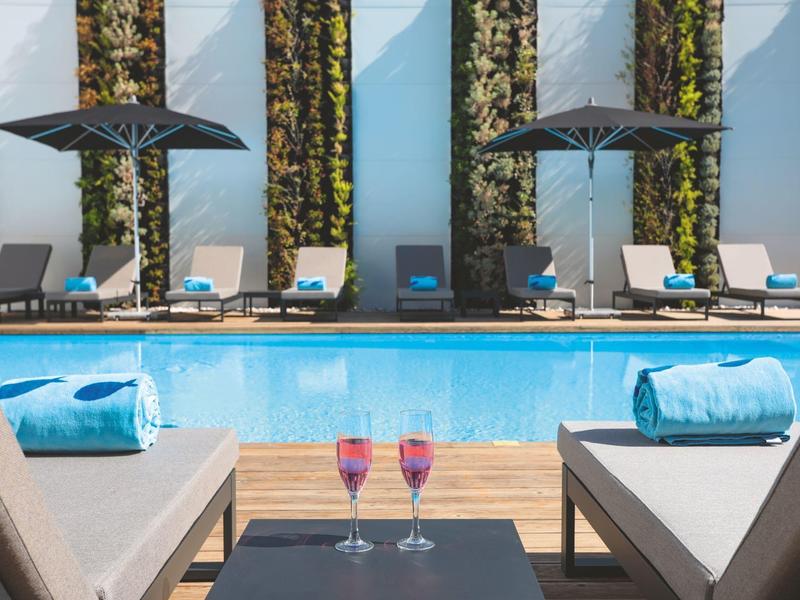 Hotel pool area with lounge chairs, umbrellas, and two drinks on a table.