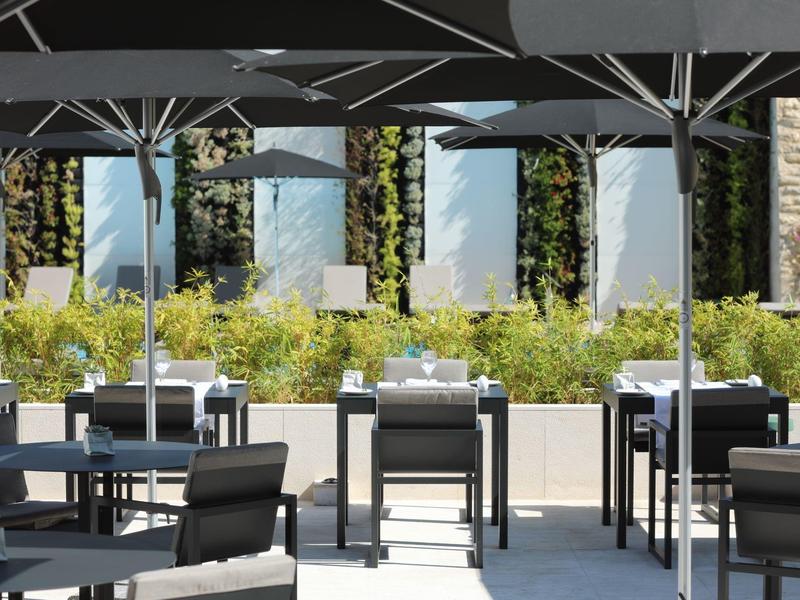 Outdoor seating area of a hotel with white tables, black chairs, and large umbrellas.