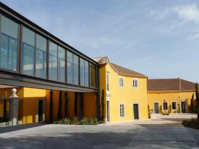 Žlutá budova hotelu s moderní skleněnou chodbou pod jasnou oblohou.