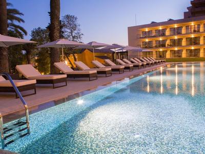 Osvětlený hotelový bazén s lehátky a slunečníky za soumraku.