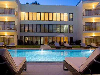 Moderní hotel s osvětleným venkovním bazénem a lehátky večer.