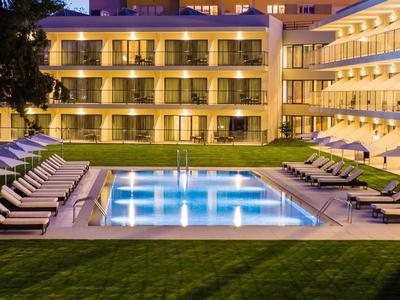 Osvětlený venkovní bazén a lehátka před hotelem v noci.