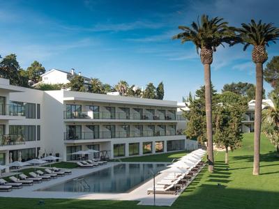 Moderní hotelový bazén s lehátky vedle bílé budovy a palem.