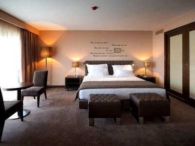 Prostorný hotelový pokoj s manželskou postelí, dvěma křesly, nočními stolky a velkou skříní.