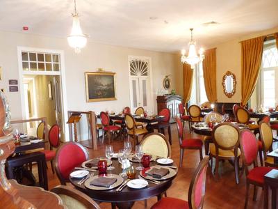 Elegantní jídelna s kulatými stoly, červenými a béžovými židlemi, teplými závěsy a lustry.