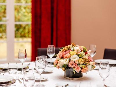 Elegantní stůl s květinovou dekorací a sklenicemi před červenými závěsy.