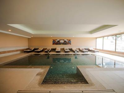 Vnitřní bazén s lehátky a velkými okny v klidném hotelovém spa.