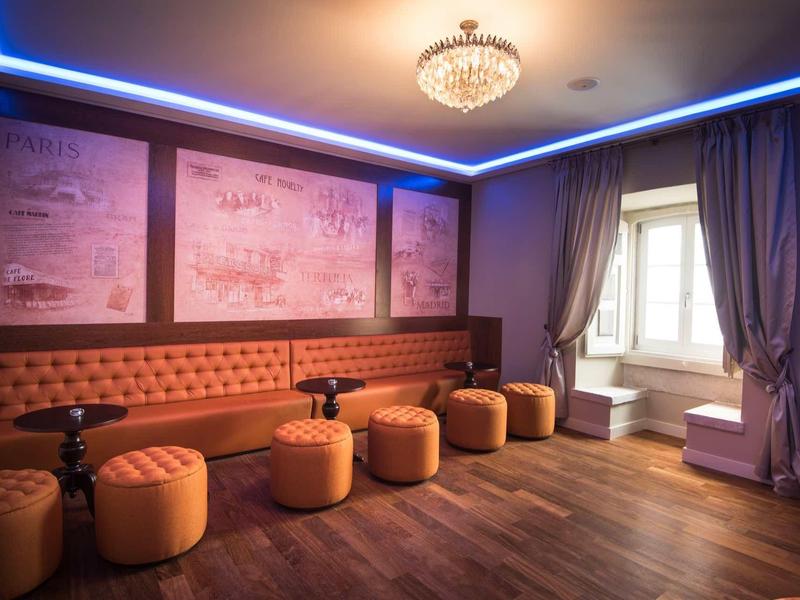 Útulná hotelová společenská místnost s červenými stolky, dřevěnou podlahou a lustr.