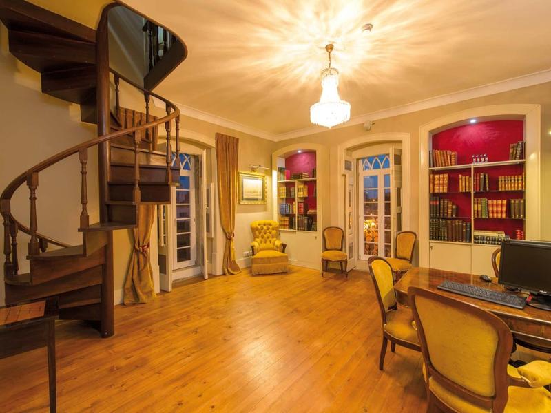 Elegantní hotelový čtecí pokoj s dřevěnou podlahou, točitým schodištěm a klasickými křesly.