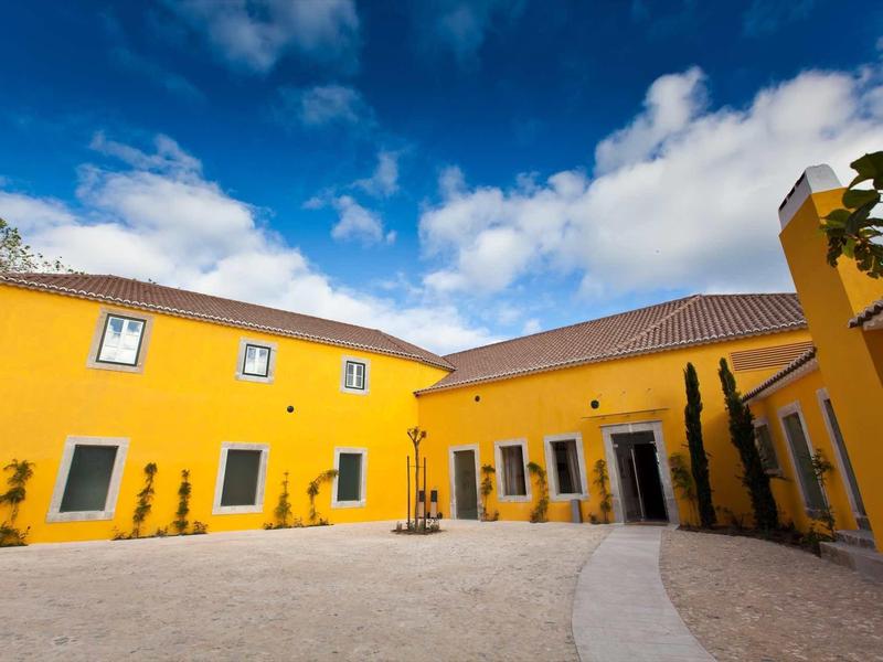 Žlutá hotelová budova s vnitřním dvorem a modrou oblohou za slunečného počasí.