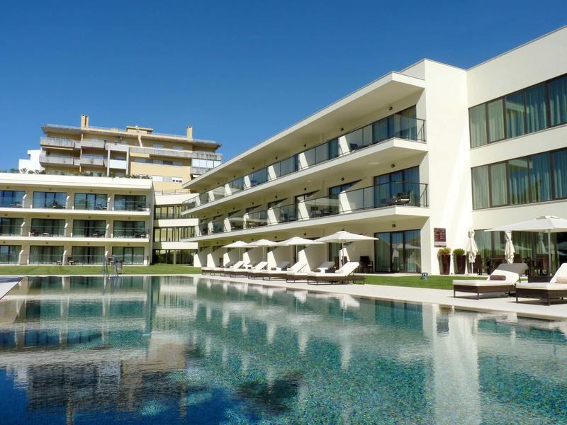 Moderní hotelový komplex s velkým venkovním bazénem a slunečníky pod jasnou oblohou