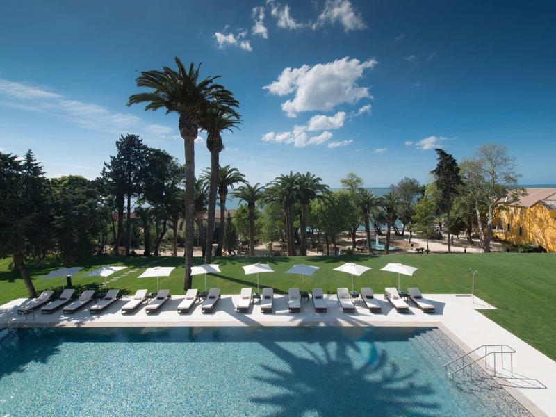 Velký bazén s lehátky a palmami pod modrou oblohou