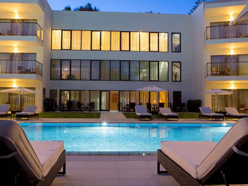 Moderní hotel s osvětleným venkovním bazénem a lehátky večer.