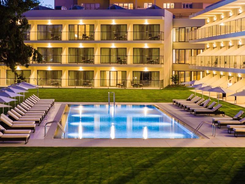 Osvětlený venkovní bazén a lehátka před hotelem v noci.