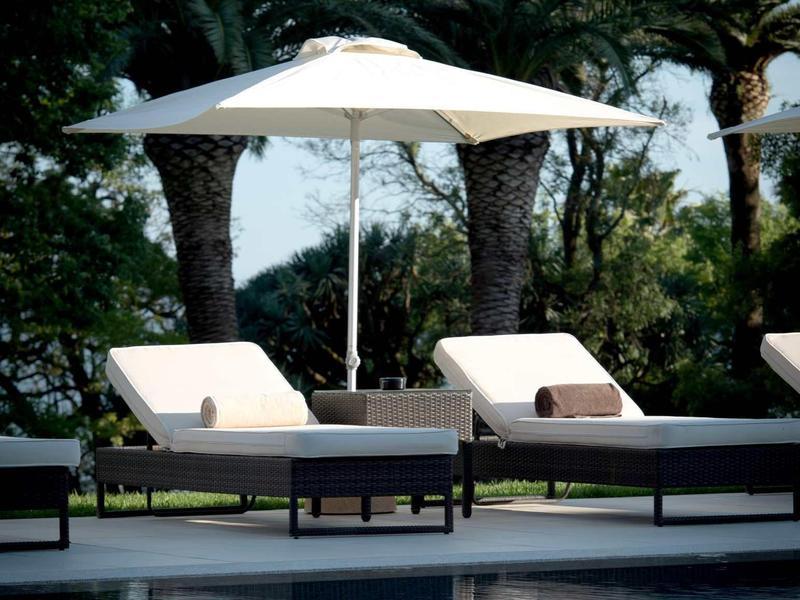 Lehátka u bazénu se slunečníkem před palmami za slunečného dne