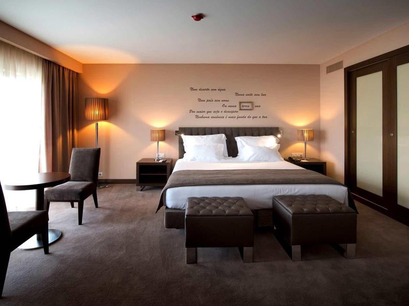 Prostorný hotelový pokoj s manželskou postelí, dvěma křesly, nočními stolky a velkou skříní.