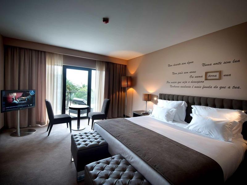 Moderní hotelový pokoj se dvojlůžkem, TV, posezením a oknem s výhledem do zeleně.