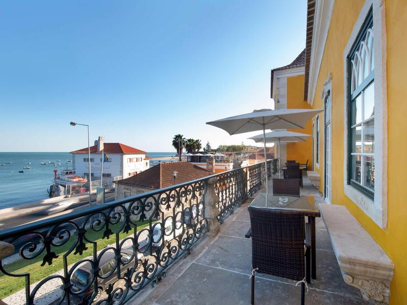 Balkon se židlemi a slunečníky s výhledem na moře a oblohu.