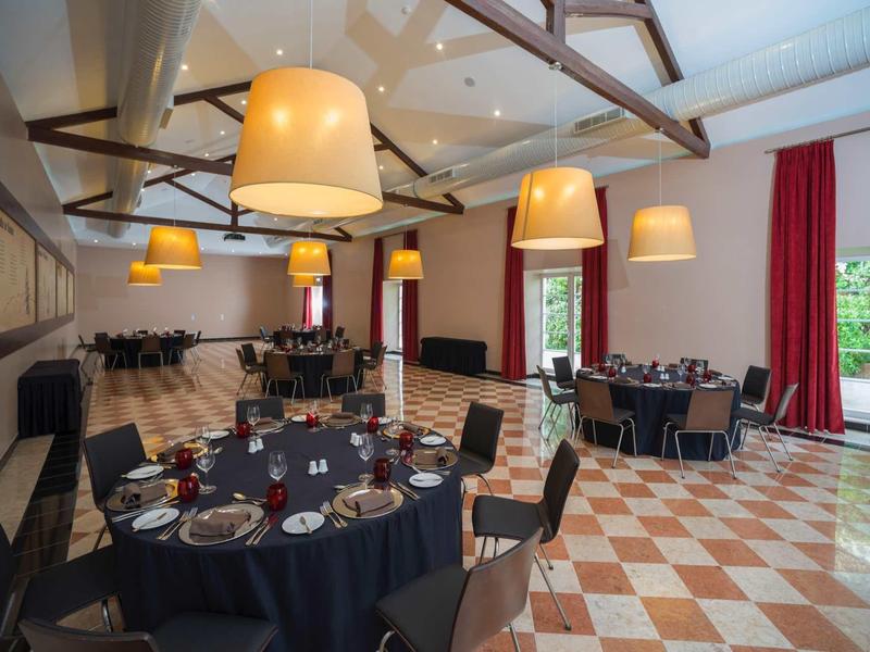 Elegantní jídelna s kulatými stoly, černými ubrusy a velkými lampami nad stoly.