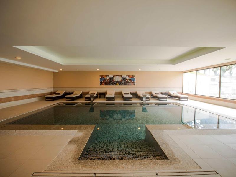 Vnitřní bazén s lehátky a velkými okny v klidném hotelovém spa.