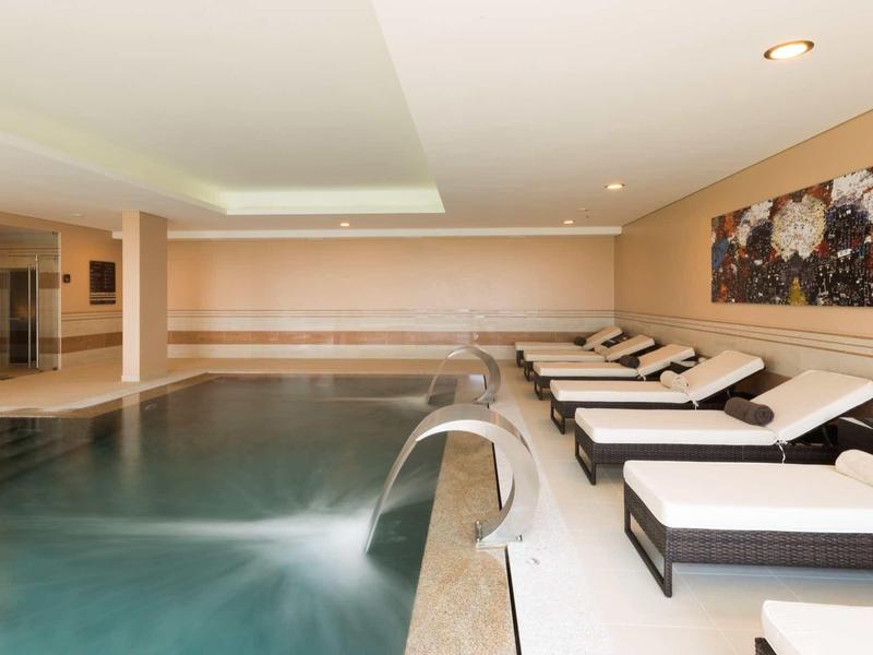 Vnitřní bazén s vodopádem a lehátky v moderním wellness centru.