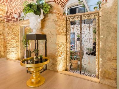 Interno luminoso con muro in pietra, cancello decorativo in metallo e tavolo dorato con piante.