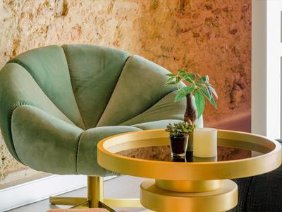 Poltrona in velluto verde accanto a tavolo rotondo dorato su parete strutturata in camera d'hotel.