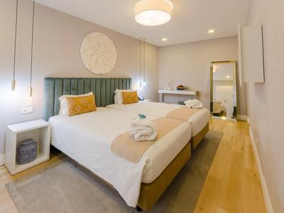 Camera d'hotel moderna con letto matrimoniale, testiera imbottita verde e accenti in legno caldo.