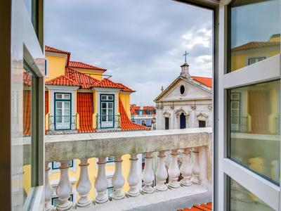 Vista da una finestra aperta su un balcone con balaustra e edifici storici con tetti rossi.