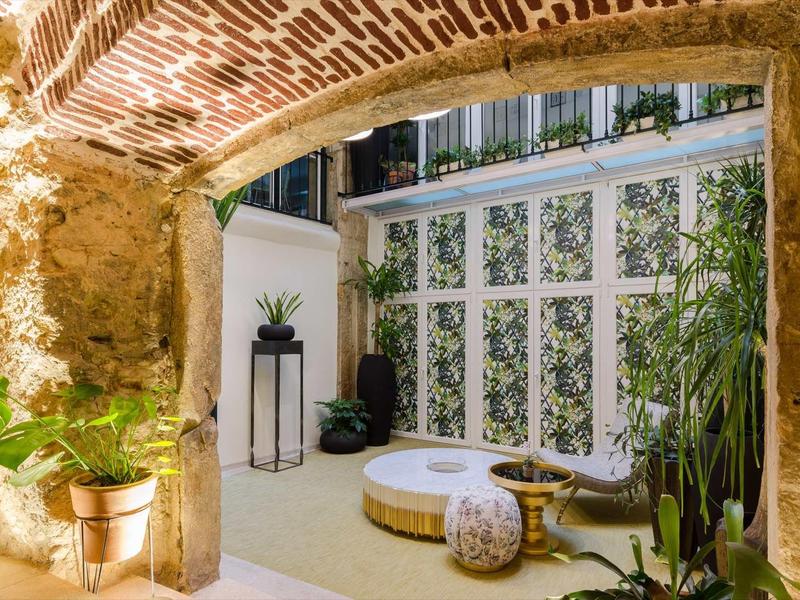 Cortile accogliente con texture erbosa, piante e area salotto sotto un arco in mattoni.