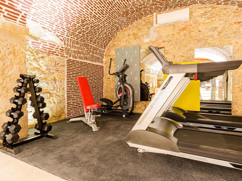 Sala allenamento con tapis roulant, rastrelliera per manubri, panca e attrezzo fitness in una stanza con muri in pietra.