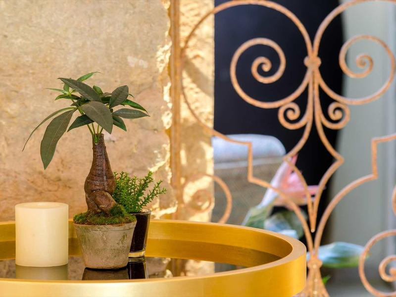 Tavolo rotondo giallo con piante e candela davanti a ringhiera metallica decorativa in un hotel.