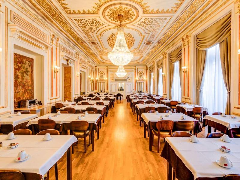 Grande sala da pranzo elegante con accenti dorati e lampadari in un hotel.