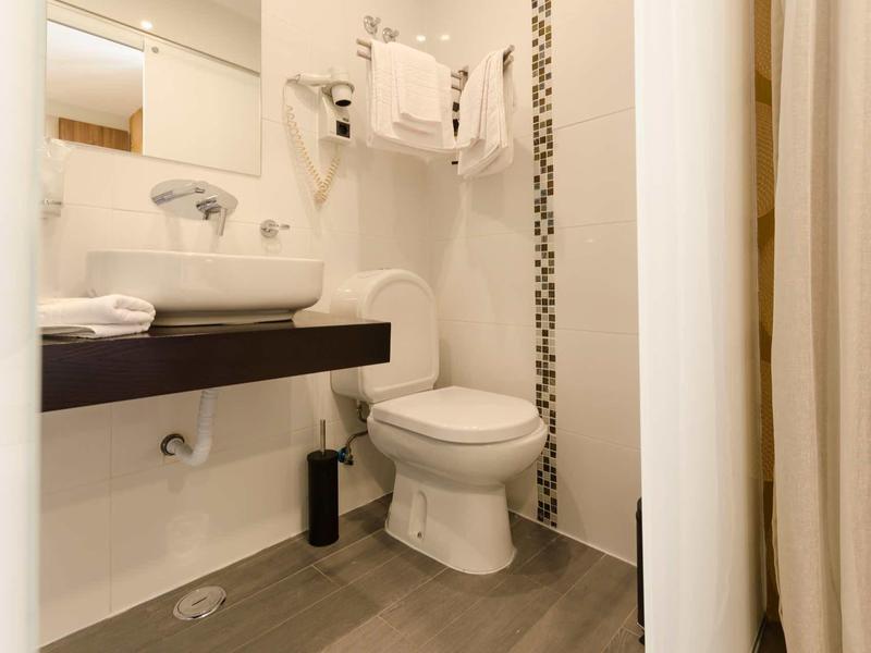 Bagno compatto con wc bianco, lavabo, grande specchio e asciugacapelli.