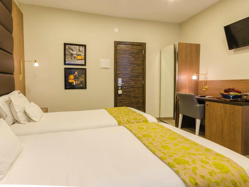 Camera d'hotel moderna con due letti, scrivania, TV e illuminazione calda.