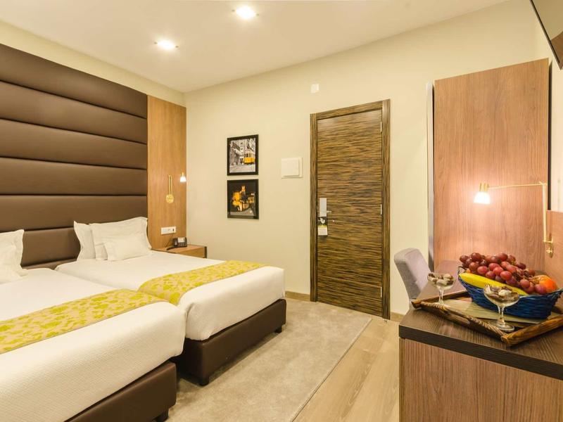 Camera d'hotel luminosa con due letti singoli, mobili in legno e illuminazione moderna.